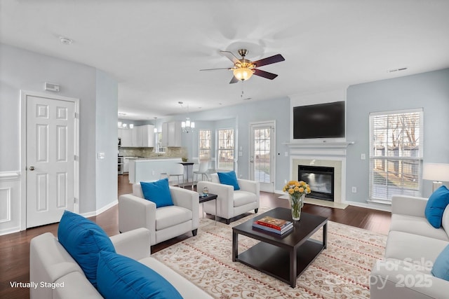 living room with ceiling fan with notable chandelier, hardwood / wood-style floors, and a high end fireplace