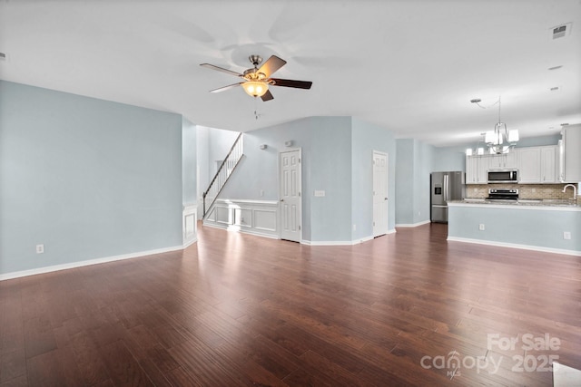 unfurnished living room featuring ceiling fan with notable chandelier and dark hardwood / wood-style floors