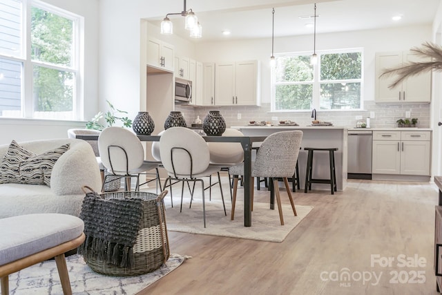 kitchen featuring appliances with stainless steel finishes, white cabinets, hanging light fixtures, and light hardwood / wood-style flooring