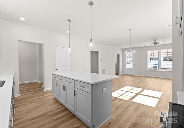 kitchen featuring light wood-type flooring, gray cabinets, a kitchen island, and pendant lighting