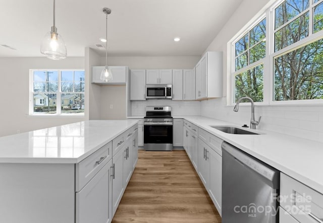 kitchen featuring tasteful backsplash, stainless steel appliances, white cabinets, pendant lighting, and sink