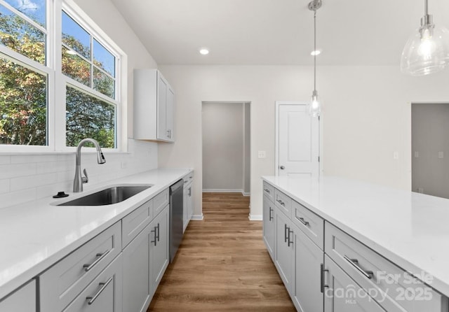 kitchen featuring hanging light fixtures, light hardwood / wood-style flooring, sink, and stainless steel dishwasher