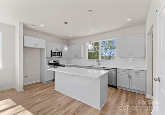 kitchen with hanging light fixtures, stainless steel appliances, a center island, backsplash, and sink