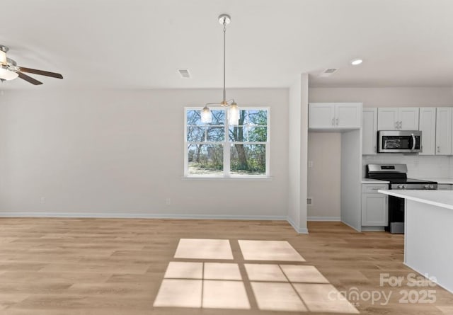 kitchen with hanging light fixtures, light hardwood / wood-style floors, backsplash, appliances with stainless steel finishes, and white cabinets