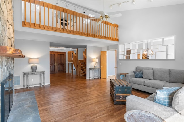 living room with hardwood / wood-style floors, a towering ceiling, a fireplace, and ceiling fan with notable chandelier