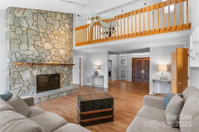 living room with rail lighting, a towering ceiling, a fireplace, and light hardwood / wood-style floors