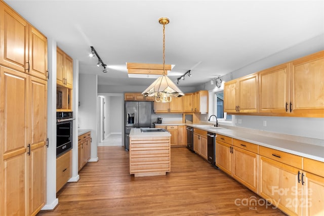 kitchen featuring sink, hanging light fixtures, a center island, black appliances, and light wood-type flooring