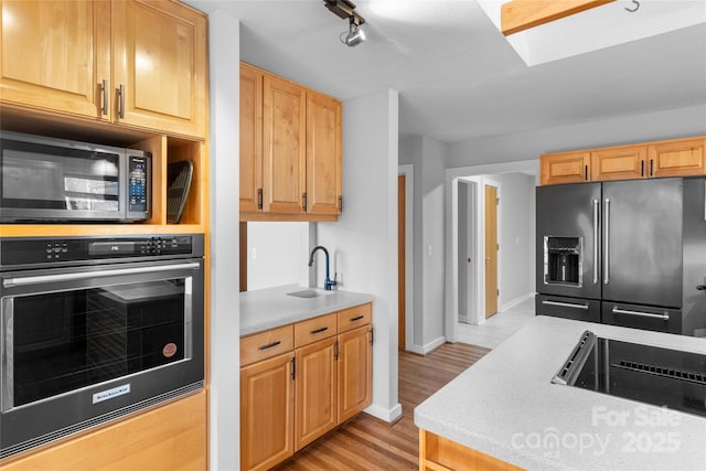 kitchen with sink, wall oven, high end black refrigerator, light wood-type flooring, and light brown cabinets