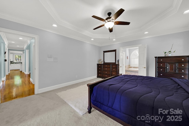 carpeted bedroom featuring a raised ceiling, ornamental molding, ensuite bathroom, and ceiling fan