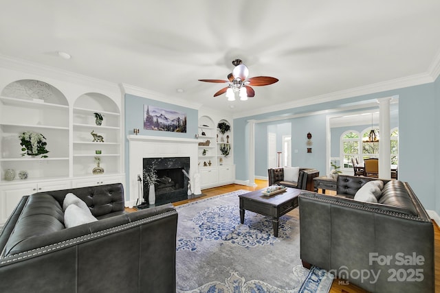 living room with a premium fireplace, ceiling fan, wood-type flooring, ornamental molding, and built in shelves