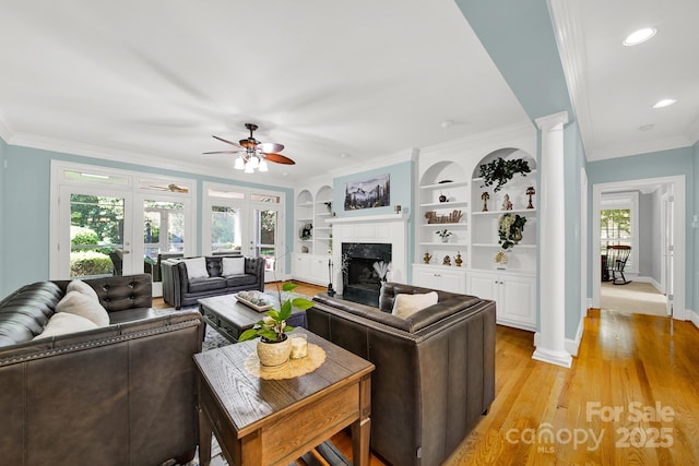 living room with light hardwood / wood-style flooring, built in features, a premium fireplace, ornamental molding, and ornate columns