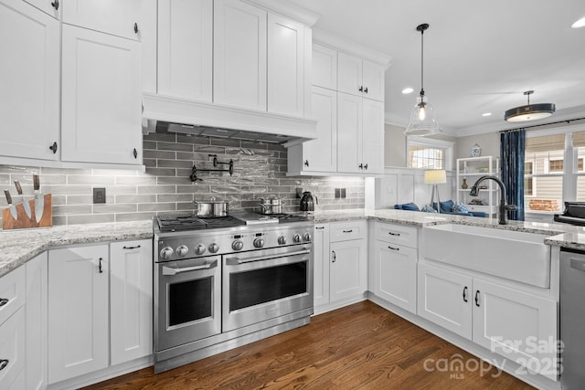 kitchen with sink, hanging light fixtures, custom range hood, stainless steel appliances, and white cabinets