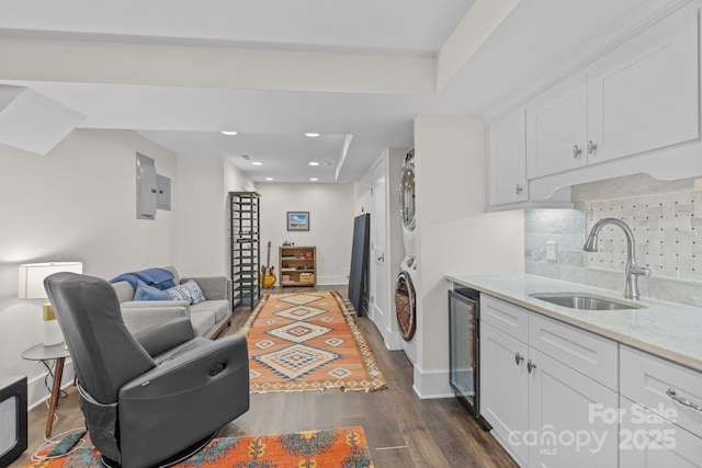 kitchen with white cabinetry, stacked washer / drying machine, dark hardwood / wood-style flooring, and sink