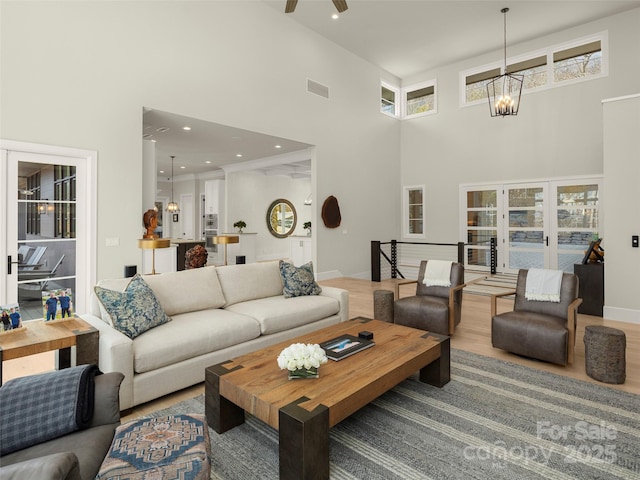 living room featuring a towering ceiling, a chandelier, hardwood / wood-style flooring, plenty of natural light, and french doors