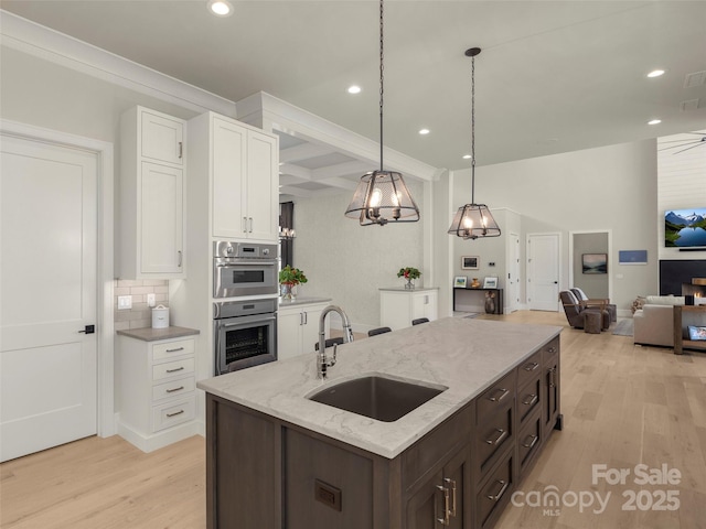 kitchen featuring sink, white cabinetry, dark brown cabinetry, light stone counters, and decorative light fixtures