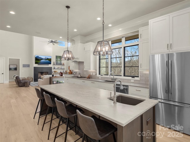 kitchen featuring pendant lighting, an island with sink, sink, white cabinets, and stainless steel appliances