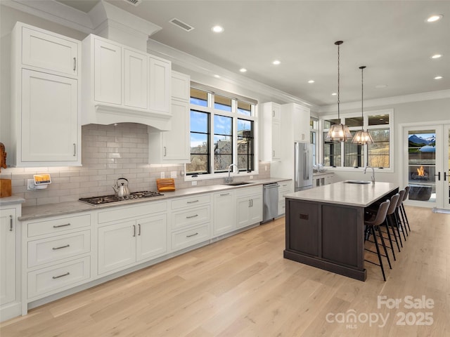 kitchen with appliances with stainless steel finishes, pendant lighting, sink, white cabinets, and a center island with sink