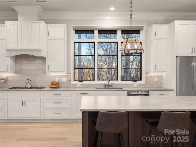 kitchen featuring appliances with stainless steel finishes, sink, a breakfast bar area, white cabinets, and hanging light fixtures