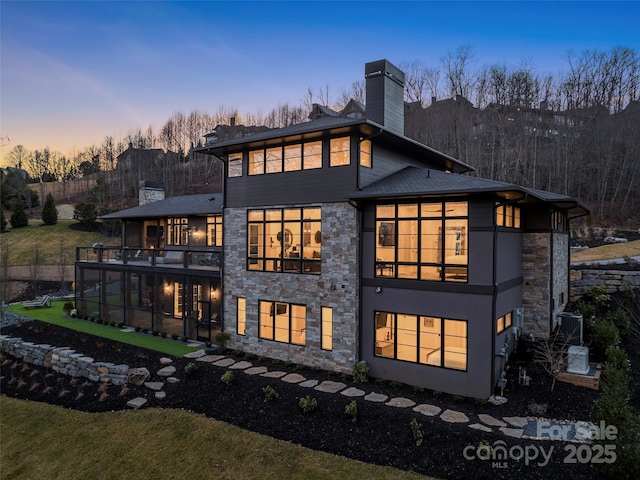 back house at dusk featuring a lawn and a balcony