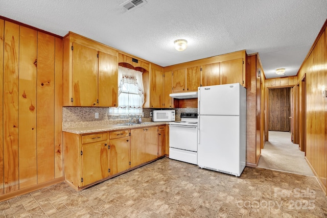 kitchen with sink, white appliances, backsplash, a textured ceiling, and wood walls