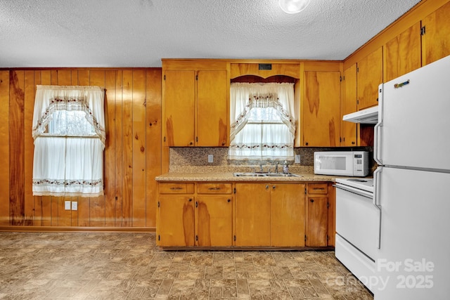 kitchen with sink, wood walls, a textured ceiling, white appliances, and backsplash