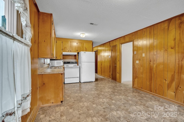 kitchen featuring white appliances, a textured ceiling, and wood walls