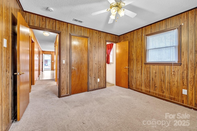 unfurnished bedroom featuring ceiling fan, a textured ceiling, light carpet, a closet, and wood walls