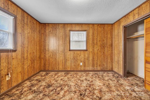 unfurnished bedroom featuring a closet, wooden walls, carpet, and a textured ceiling