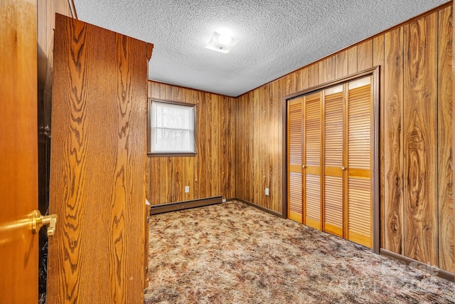 unfurnished bedroom with wooden walls, carpet floors, a textured ceiling, a baseboard radiator, and a closet