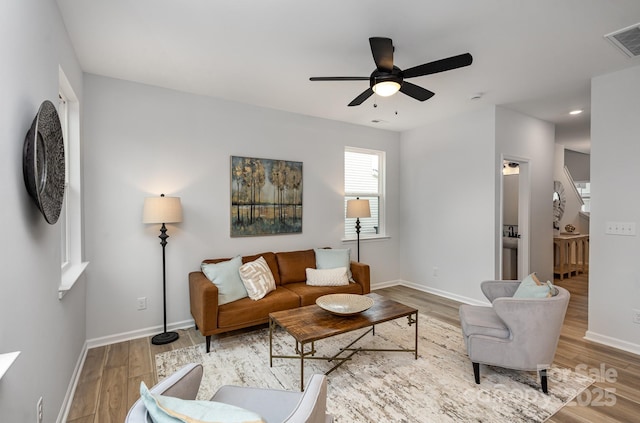 living area featuring ceiling fan, light wood finished floors, visible vents, and baseboards