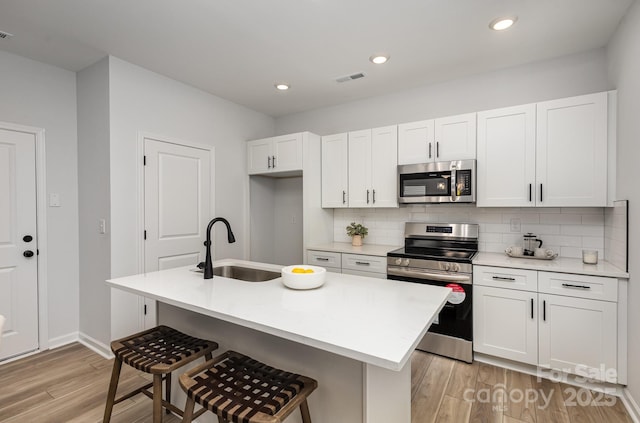 kitchen featuring stainless steel appliances, light countertops, a kitchen island with sink, white cabinets, and a sink