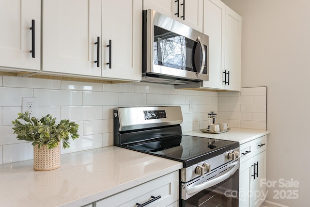 kitchen featuring stainless steel appliances, white cabinetry, light stone counters, and tasteful backsplash