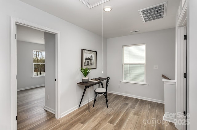 hallway featuring light wood finished floors, attic access, visible vents, and baseboards