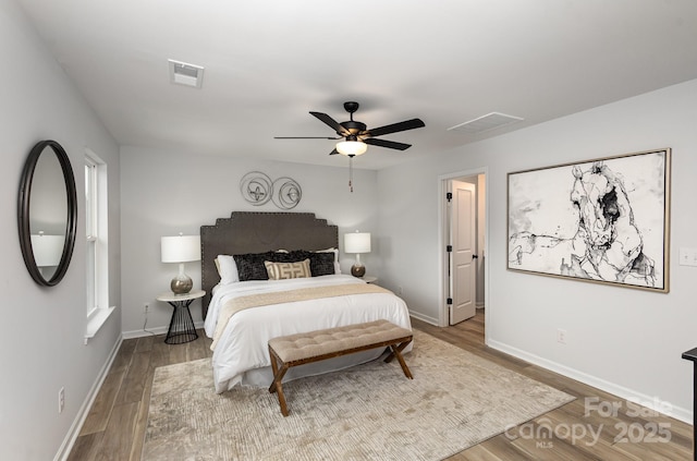 bedroom with a ceiling fan, visible vents, baseboards, and wood finished floors