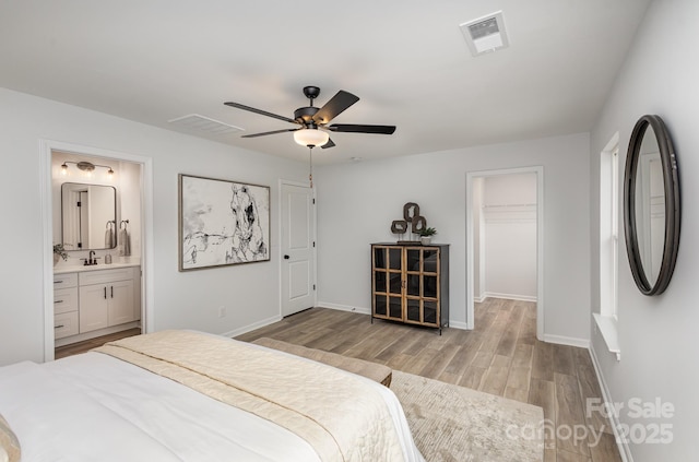 bedroom featuring visible vents, light wood-style flooring, a spacious closet, a sink, and baseboards