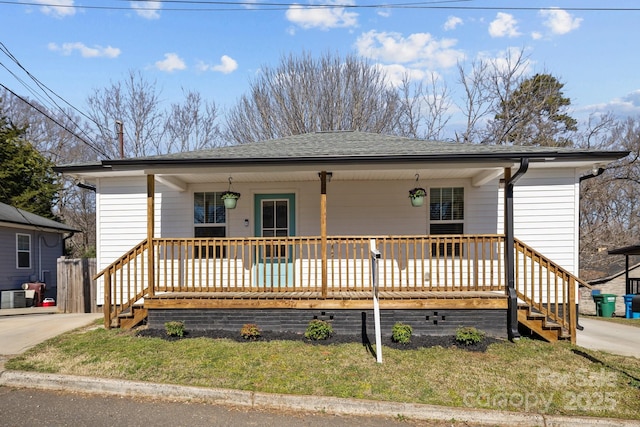 view of front facade featuring central air condition unit, roof with shingles, a porch, and a front yard