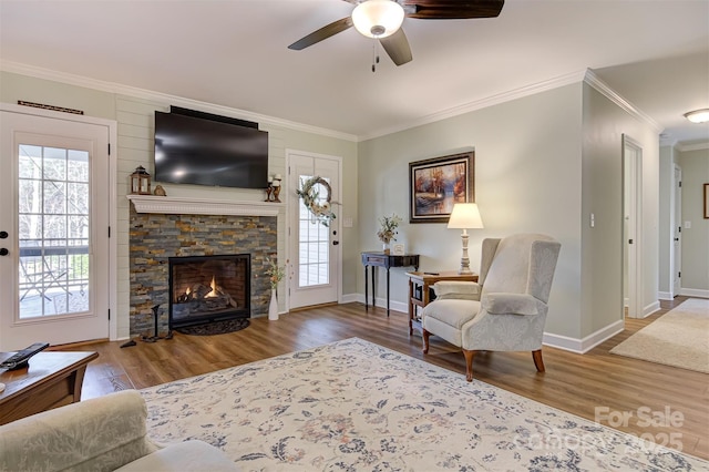 living room with crown molding, ceiling fan, wood-type flooring, and a fireplace