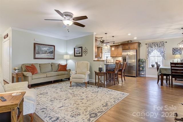 living room with crown molding, sink, ceiling fan with notable chandelier, and light hardwood / wood-style floors