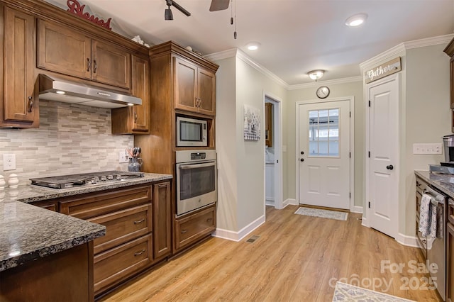 kitchen with dark stone countertops, decorative backsplash, light hardwood / wood-style floors, stainless steel appliances, and crown molding