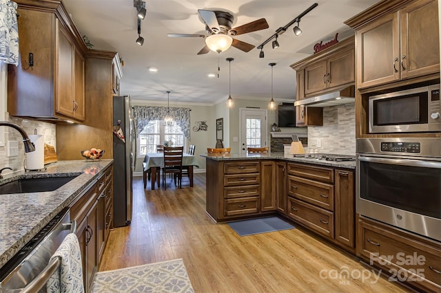 kitchen featuring sink, appliances with stainless steel finishes, hanging light fixtures, dark stone counters, and light wood-type flooring