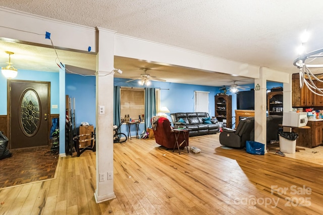 living room featuring ceiling fan, light hardwood / wood-style flooring, a textured ceiling, and ornate columns