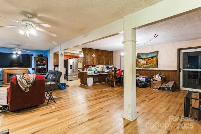 living room featuring ornate columns, wooden walls, ceiling fan, light hardwood / wood-style floors, and a textured ceiling