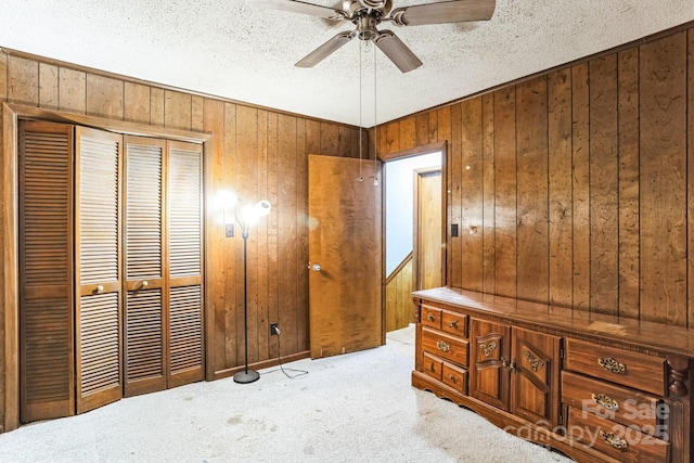 carpeted bedroom with ceiling fan, wooden walls, a textured ceiling, and a closet