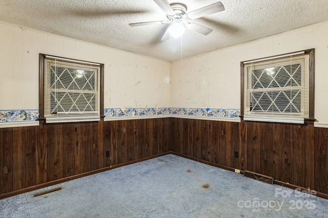 unfurnished room with ceiling fan, light carpet, a textured ceiling, and wood walls