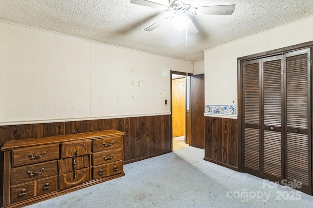 carpeted bedroom with ceiling fan, a closet, wooden walls, and a textured ceiling