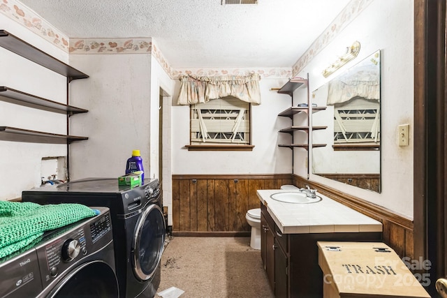 interior space featuring wood walls, vanity, toilet, washing machine and dryer, and a textured ceiling