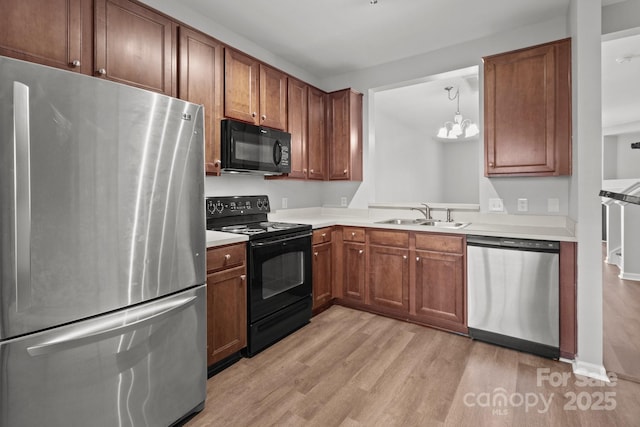 kitchen featuring sink, light hardwood / wood-style flooring, a notable chandelier, black appliances, and decorative light fixtures