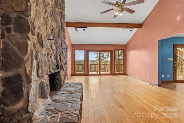 unfurnished living room featuring ceiling fan, a fireplace, a textured ceiling, beamed ceiling, and light wood-type flooring