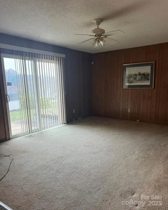 empty room with wooden walls, ceiling fan, carpet flooring, and a textured ceiling