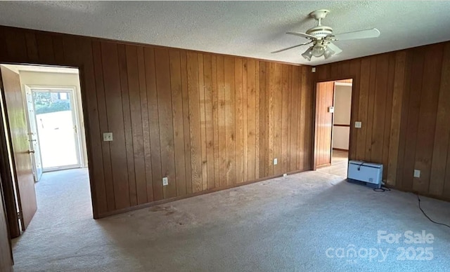 unfurnished room featuring ceiling fan, a textured ceiling, light carpet, and wood walls